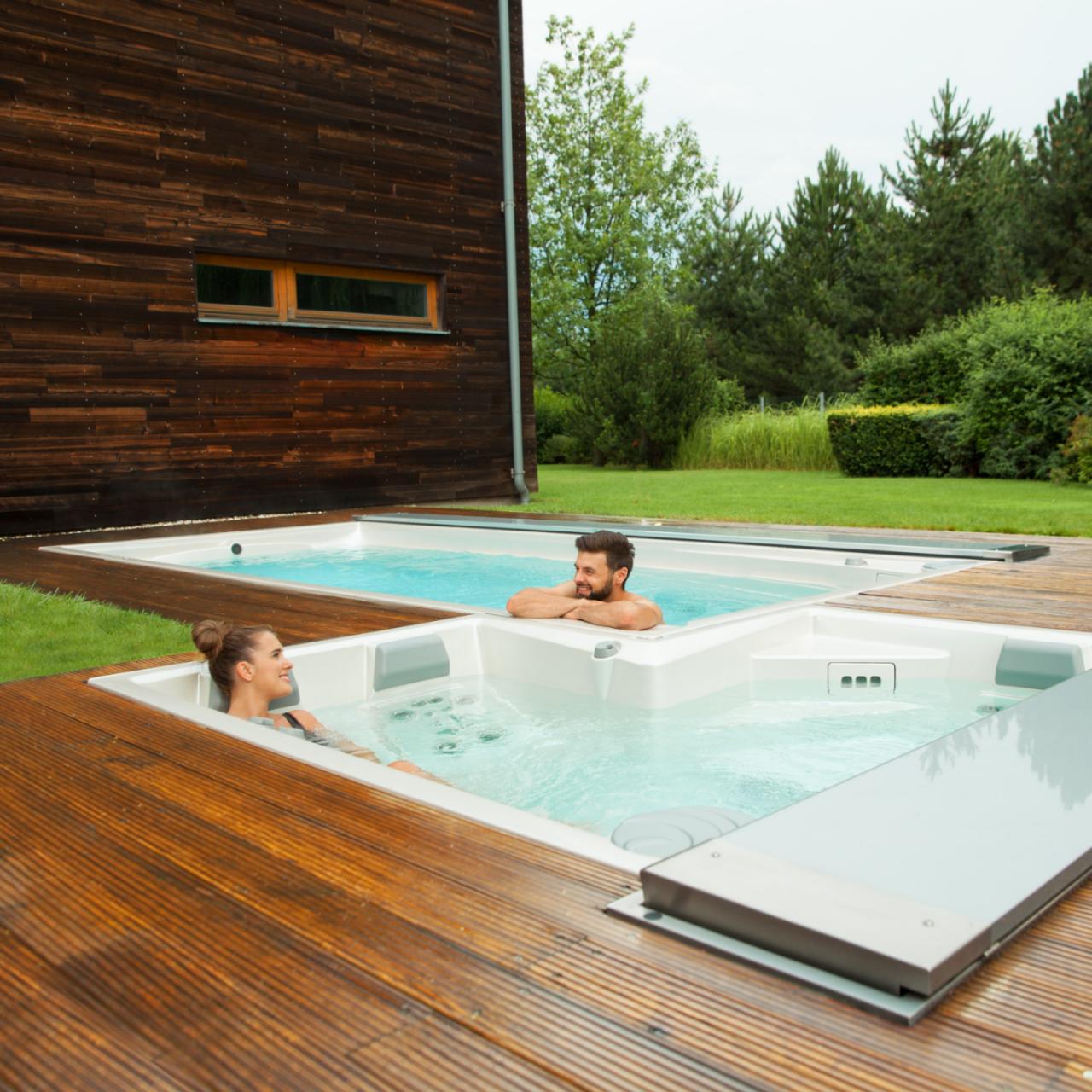 Pár pihen a szabadtéri USSPA wellness- és úszómedencékben, melyeket egy fa teraszra építettek.